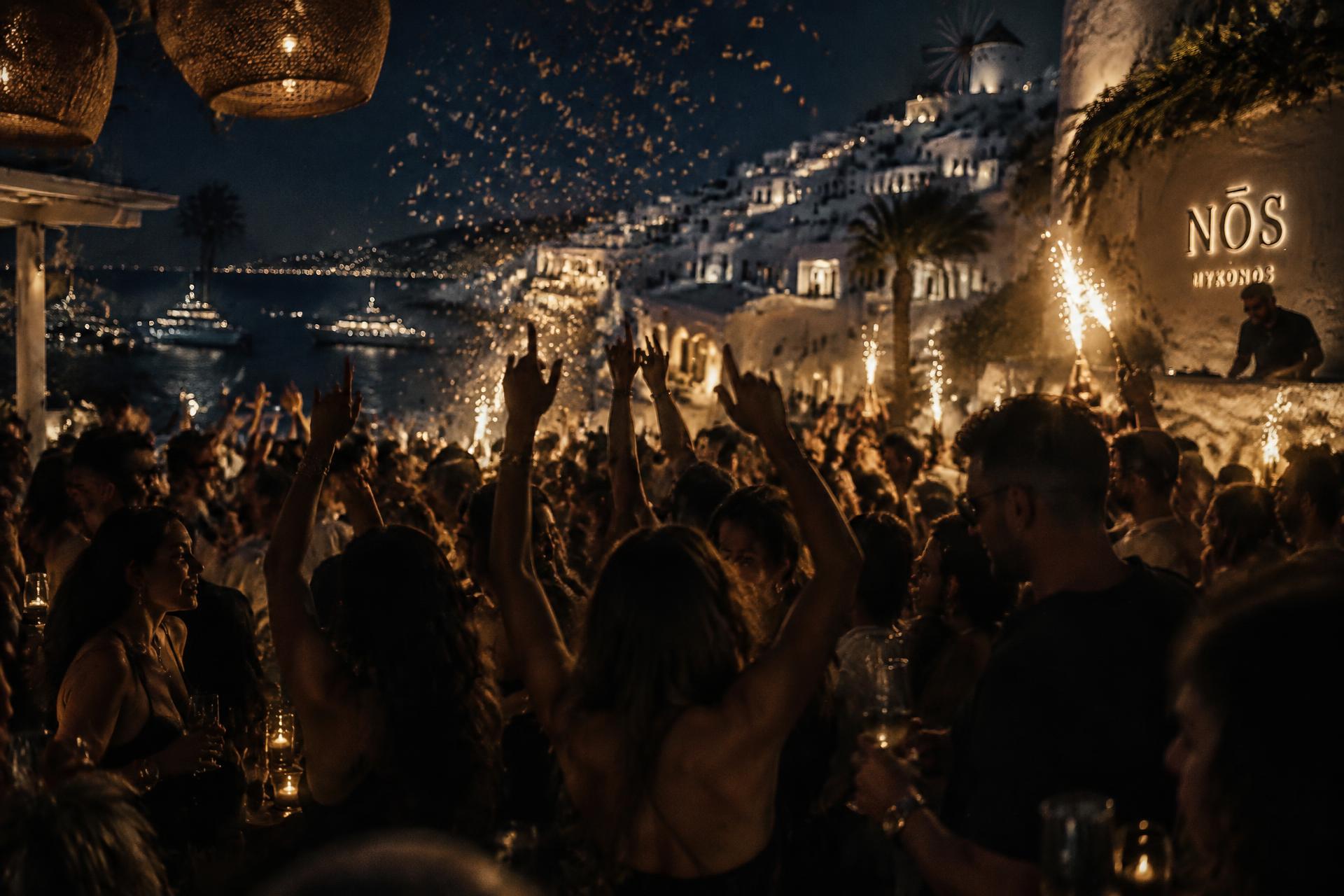 Packed open-air Greek island club at night, confetti falling over the dancefloor
